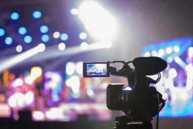 Profesyonel video kamera canlı bir konser ya da etkinlik kaydediyor, sahneyi gösteren bir ekran ve arka planda parlak renkli ışıklar. 22.05.2025 Valmiera, Letonya