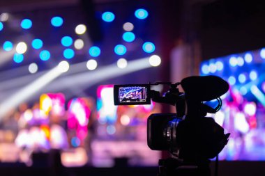 Profesyonel video kamera canlı bir konser ya da etkinlik kaydediyor, sahneyi gösteren bir ekran ve arka planda parlak renkli ışıklar. 22.05.2025 Valmiera, Letonya
