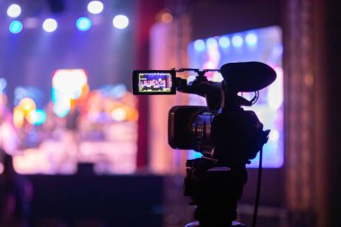 Profesyonel video kamera canlı bir konser ya da etkinlik kaydediyor, sahneyi gösteren bir ekran ve arka planda parlak renkli ışıklar. 22.05.2025 Valmiera, Letonya