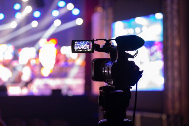 Profesyonel video kamera canlı bir konser ya da etkinlik kaydediyor, sahneyi gösteren bir ekran ve arka planda parlak renkli ışıklar. 22.05.2025 Valmiera, Letonya
