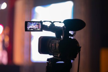 Profesyonel video kamera canlı bir konser ya da etkinlik kaydediyor, sahneyi gösteren bir ekran ve arka planda parlak renkli ışıklar. 22.05.2025 Valmiera, Letonya
