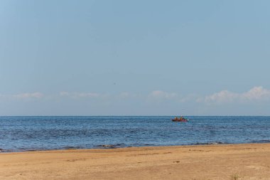 Açık mavi gökyüzünün altında, açık mavi bulutlar ve uçan martılarla sakin bir denizdeki insanların olduğu uzak bir motorlu tekne..