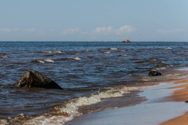 Güneş ışığı altında kıyıya yaklaşan küçük köpüklü bir dalganın yakın çekimi, koyu mavi sudaki dalgalanmaları ve dokuları vurguluyor..