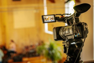 Profesyonel bir Sony 4K video kamerasının üç ayaklı bir kamera ile yakın plan çekimleri. İçeriden hafif ışıklandırılmış, odak dışı bir arka plan..