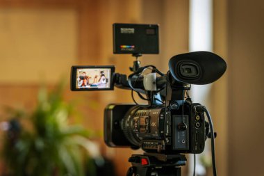 Profesyonel bir Sony 4K video kamerasının üç ayaklı bir kamera ile yakın plan çekimleri. İçeriden hafif ışıklandırılmış, odak dışı bir arka plan..