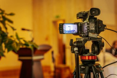 Profesyonel bir Sony 4K video kamerasının üç ayaklı bir kamera ile yakın plan çekimleri. İçeriden hafif ışıklandırılmış, odak dışı bir arka plan..