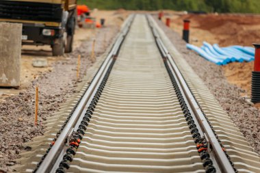 Uzun, düz tren yolları bulutlu bir gökyüzü altında yeşil orman alanlarının arasına kadar uzanıyor ve güçlü bir perspektif ve simetri sunuyor..