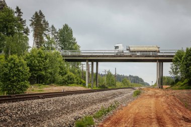 Uzun, düz tren yolları bulutlu bir gökyüzü altında yeşil orman alanlarının arasına kadar uzanıyor ve güçlü bir perspektif ve simetri sunuyor..