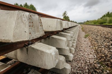 Düzgün istiflenmiş beton ve çelik demiryolu bölümleri yeşil ağaçlar ve bulutlu gökyüzü ile çevrili aktif bir demiryolu hattı boyunca konumlandırılmıştır..