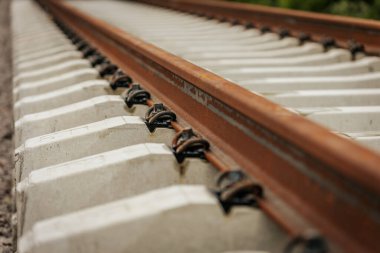 Düzgün istiflenmiş beton ve çelik demiryolu bölümleri yeşil ağaçlar ve bulutlu gökyüzü ile çevrili aktif bir demiryolu hattı boyunca konumlandırılmıştır..