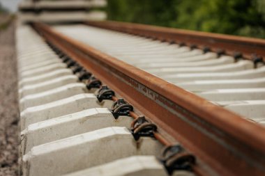 Düzgün istiflenmiş beton ve çelik demiryolu bölümleri yeşil ağaçlar ve bulutlu gökyüzü ile çevrili aktif bir demiryolu hattı boyunca konumlandırılmıştır..
