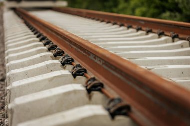 Düzgün istiflenmiş beton ve çelik demiryolu bölümleri yeşil ağaçlar ve bulutlu gökyüzü ile çevrili aktif bir demiryolu hattı boyunca konumlandırılmıştır..