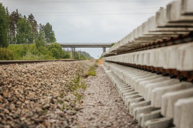 Düzgün istiflenmiş beton ve çelik demiryolu bölümleri yeşil ağaçlar ve bulutlu gökyüzü ile çevrili aktif bir demiryolu hattı boyunca konumlandırılmıştır..