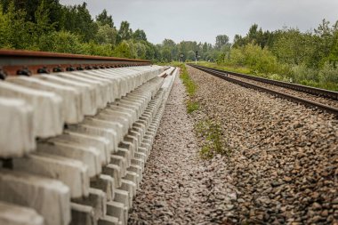 Düzgün istiflenmiş beton ve çelik demiryolu bölümleri yeşil ağaçlar ve bulutlu gökyüzü ile çevrili aktif bir demiryolu hattı boyunca konumlandırılmıştır..