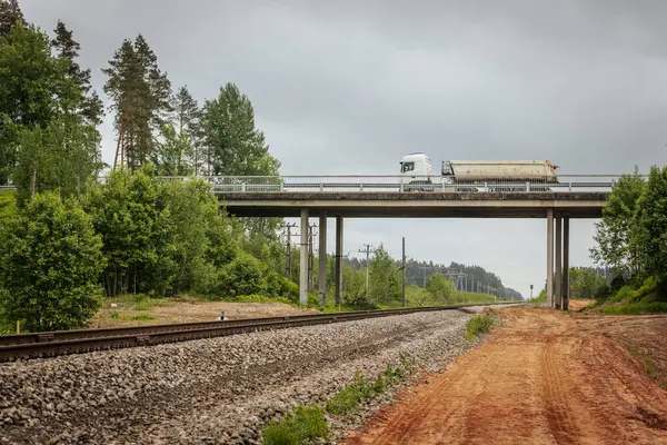 Uzun, düz tren yolları bulutlu bir gökyüzü altında yeşil orman alanlarının arasına kadar uzanıyor ve güçlü bir perspektif ve simetri sunuyor..