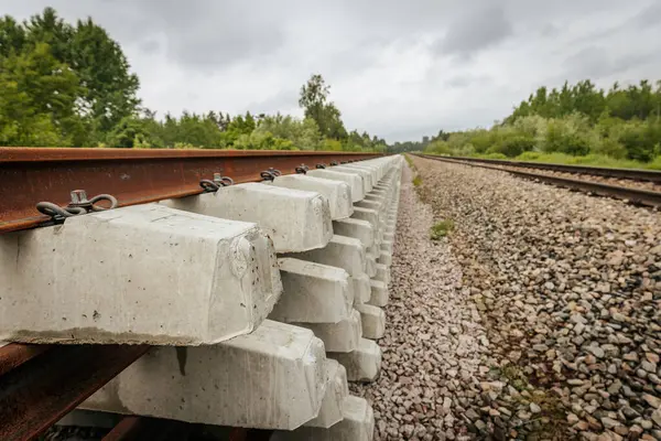 Düzgün istiflenmiş beton ve çelik demiryolu bölümleri yeşil ağaçlar ve bulutlu gökyüzü ile çevrili aktif bir demiryolu hattı boyunca konumlandırılmıştır..