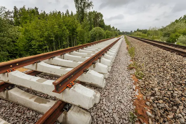 Düzgün istiflenmiş beton ve çelik demiryolu bölümleri yeşil ağaçlar ve bulutlu gökyüzü ile çevrili aktif bir demiryolu hattı boyunca konumlandırılmıştır..