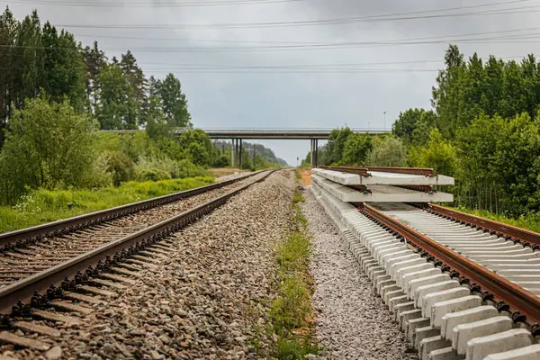 Düzgün istiflenmiş beton ve çelik demiryolu bölümleri yeşil ağaçlar ve bulutlu gökyüzü ile çevrili aktif bir demiryolu hattı boyunca konumlandırılmıştır..