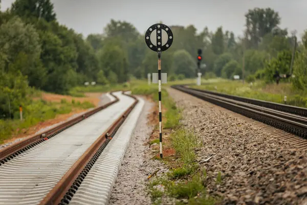 Düzgün istiflenmiş beton ve çelik demiryolu bölümleri yeşil ağaçlar ve bulutlu gökyüzü ile çevrili aktif bir demiryolu hattı boyunca konumlandırılmıştır..