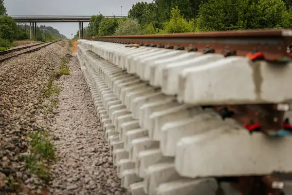Düzgün istiflenmiş beton ve çelik demiryolu bölümleri yeşil ağaçlar ve bulutlu gökyüzü ile çevrili aktif bir demiryolu hattı boyunca konumlandırılmıştır..