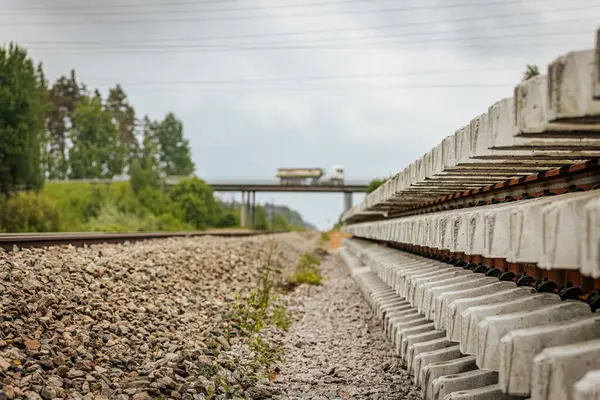 Düzgün istiflenmiş beton ve çelik demiryolu bölümleri yeşil ağaçlar ve bulutlu gökyüzü ile çevrili aktif bir demiryolu hattı boyunca konumlandırılmıştır..