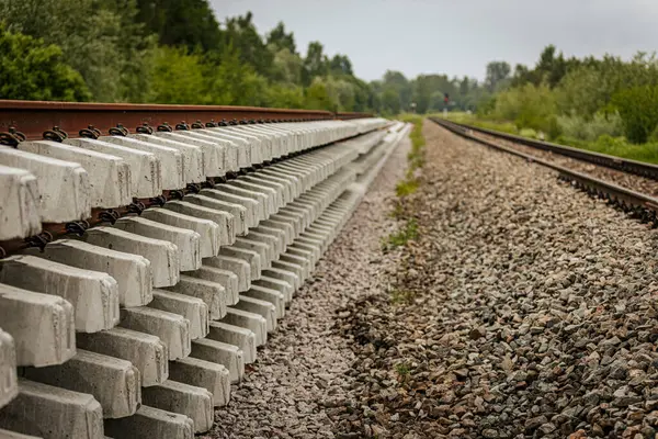 Düzgün istiflenmiş beton ve çelik demiryolu bölümleri yeşil ağaçlar ve bulutlu gökyüzü ile çevrili aktif bir demiryolu hattı boyunca konumlandırılmıştır..