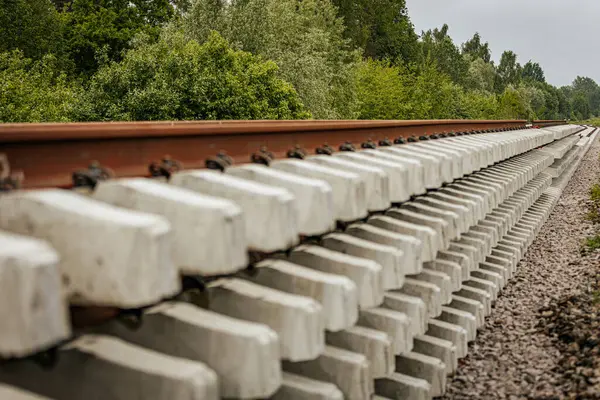 Düzgün istiflenmiş beton ve çelik demiryolu bölümleri yeşil ağaçlar ve bulutlu gökyüzü ile çevrili aktif bir demiryolu hattı boyunca konumlandırılmıştır..