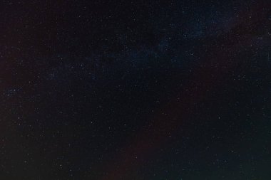 A dark sky filled with countless stars and faint aurora bands, partially covered by drifting clouds, creating a moody and mysterious celestial scene.