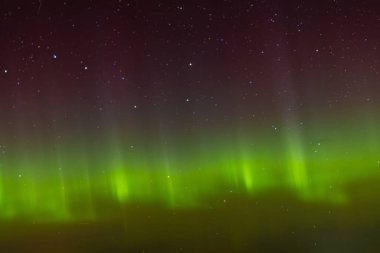 Green and red aurora lights shimmer across the star-filled night sky, creating a surreal and colorful celestial display above the horizon.