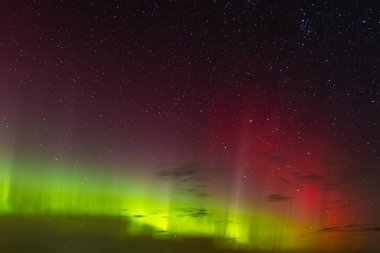 Green and red aurora lights shimmer across the star-filled night sky, creating a surreal and colorful celestial display above the horizon.