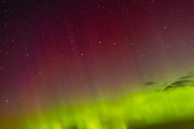 Green and red aurora lights shimmer across the star-filled night sky, creating a surreal and colorful celestial display above the horizon.