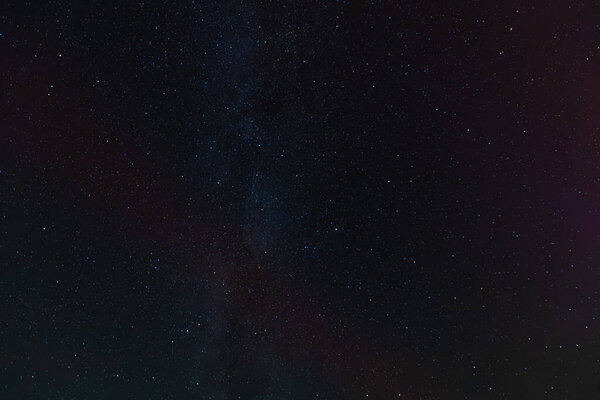 A dark sky filled with countless stars and faint aurora bands, partially covered by drifting clouds, creating a moody and mysterious celestial scene.
