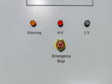 Açık hava yüksek voltajlı elektrikli dolaplar. Uyarı etiketleri, havalandırma panelleri ve açık mavi gökyüzünün altındaki acil durdurma düğmeleri..