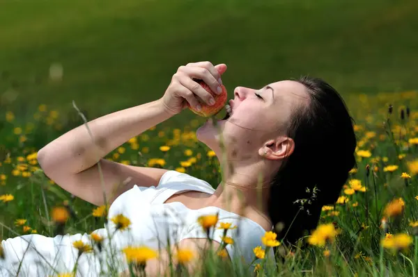 若い美しい女性は 畑に横たわっている間にリンゴを食べる — ストック写真