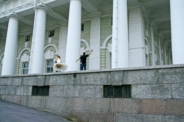 Gelin ve damat beyaz binanın yanında fotoğrafçıyla birlikte. 