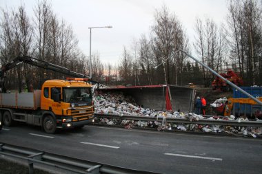 Yolda devrilmiş çöp kamyonu yakınlarında işçiler.