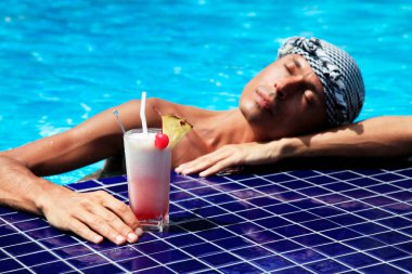 Adam havuz kenarında kokteyl içiyor.