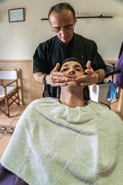 Barber extends cream in the face of the client after shaver in a barber's shop, Sabiote, Jaen province, Andalucia, Spain
