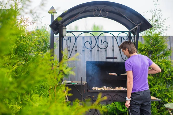 年轻男子炸薯条在户外在他的院子里烧烤牛排 — 图库照片