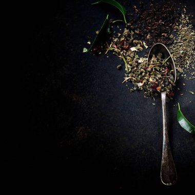 Koyu arkaplanda yeşil çay yaprakları ve kaşık