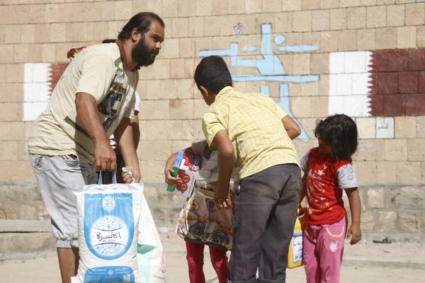 Taiz: Bir Yemenli erkek ve çocuk, 23 Ekim 2015 tarihinde Taiz 'in (Ta' izz) batısındaki Nasser okulunda yiyecek ve temiz su dağıtımı sırasında çantalar dolusu erzak taşımaktadır..