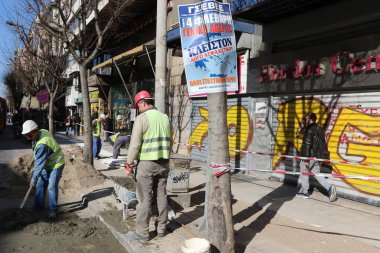 GREECE, Thessaloniki: Construction workers do work on a street in Thessaloniki, Greece on February 3, 2016, as they stand next to a flyer calling for planned nationwide strike.Public transportation is excepted to be severely disrupted