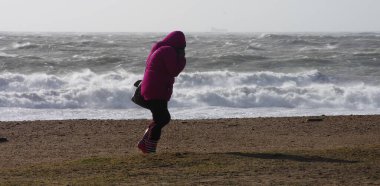 UK, Dorset: A woman faces into Storm Imogen's brutally high winds as waves crash on the south coastal beaches at Dorset, UK on February 8, 2016.