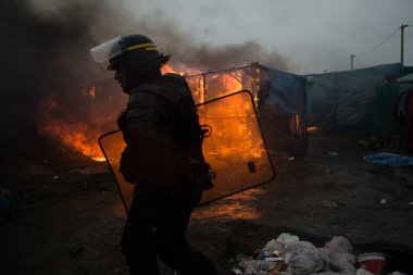 FRANCE, Calais: Göçmenler, Fransa 'nın kuzey liman kenti Calais' te 1 Mart 2016 'da kampın yarısı sökülürken, sözde Orman göçmeni kampının güney kesimindeki yanan barakaların yanından geçtiler.