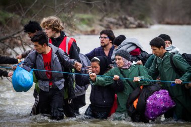 Yunanistan, Idomeni - 14 Mart 2016: Yunanistan 'ın İdomeni köyü yakınlarındaki Yunanistan-Makedonya sınırındaki derme çatma bir kamptan Makedonya' ya giden göçmenler ve mülteciler dalgalı bir nehri geçerek geçiyorlar