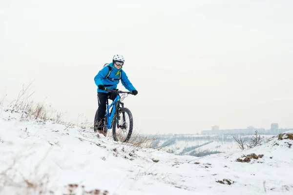 stock image Cyclist in blue resting with mountain bike on rocky winter hill. Extreme sport and enduro biking concept.