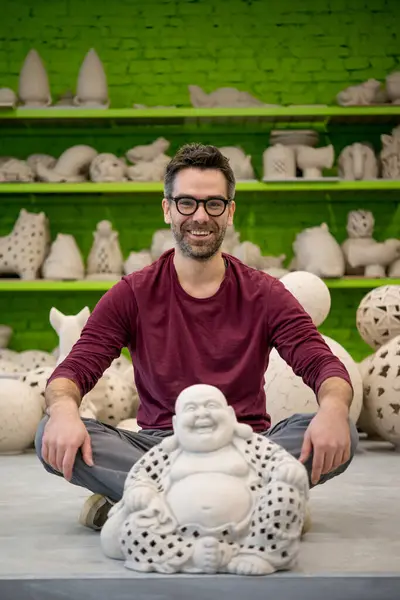 彫刻の隣に座っている明るいモダンなセラミックワークショップで笑顔のヤングセラミストの肖像 中小企業コンセプト — ストック写真