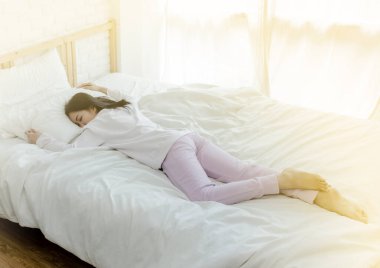 Beyaz yatakta uyuyan Asyalı kadın.