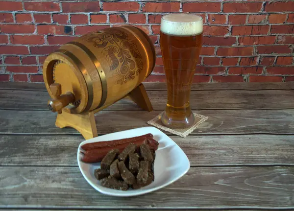 A glass of svetlog beer, a keg and a plate with snacks on roofing against the wall of red brick. Close-up.