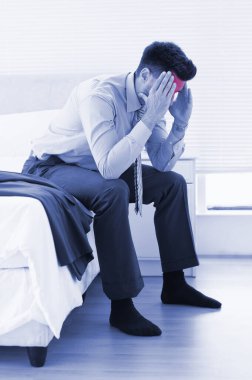 Akşamdan kalma iş adamı yatağın kenarında oturuyor. 